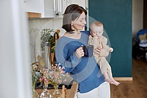 Woman holding her newborn baby and cup with tea