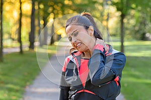 Woman holding her painful neck in park