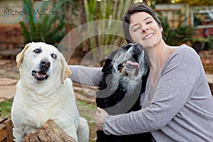 A woman holding her two Labrador dogs in a garden.
