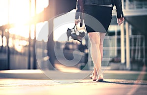 Woman holding high heels in hand and walking home from party barefoot. Businesswoman took off uncomfortable shoes. photo