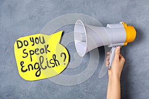 Woman holding horn and paper speech bubble with question Do You Speak English on grey background, closeup