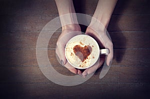 Woman holding hot cup of coffee, with heart shape