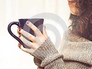 Woman holding a hot cup of coffee or tea in the morning sunlight