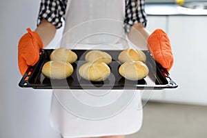 Woman holding hot roasting pan with hot, freshly baked bread rolls