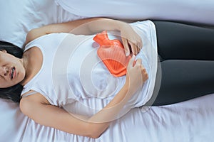Woman holding hot water bag on her stomach lying in bedroom