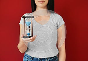 Woman holding hourglass on color background. Time management concept