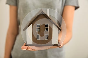 Woman holding house model on light background, closeup. Mortgage concept