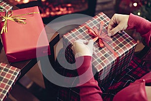 Woman holding huge gift box sitting near christmas tree and fireplace. Packing handmade christmas gifts.