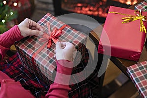 Woman holding huge gift box sitting near christmas tree and fireplace. Packing handmade christmas gifts.