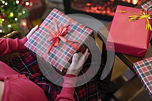 Woman holding huge gift box sitting near christmas tree and fireplace. Packing handmade christmas gifts.