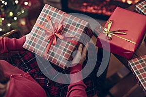 Woman holding huge gift box sitting near christmas tree and fireplace. Packing handmade christmas gifts.