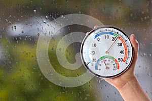Woman holding hygrometer with thermometer near window on rainy day, closeup. Space for text