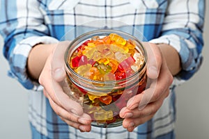 Woman holding jar of colorful jelly bears on light background