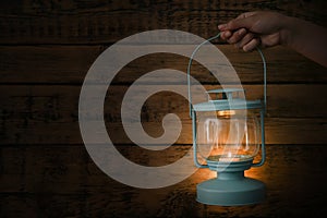 Woman holding lantern with burning candle against wooden wall in darkness, closeup. Space for text