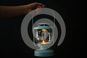 Woman holding lantern with burning candle on black background, closeup