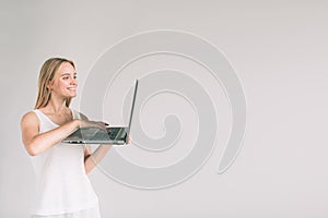 Woman holding laptop computer isolated on gray. Girl in white shirt, studio shot