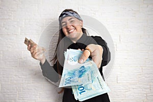 Woman holding a large amount of cash, a lot of money from Brazil offering towards the camera.