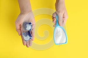 Woman holding laundry capsules and detergent powder on yellow background, top view