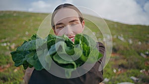 Woman holding leafy vegetables on field closeup. Happy girl posing with cabbage