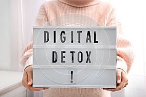 Woman holding lightbox with phrase DIGITAL DETOX at home