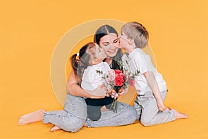 The woman is holding a little girl with flowers, and a boy is standing next to her. Children kiss mom and congratulate her on the
