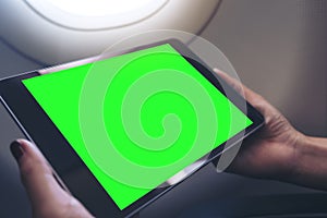 A woman holding and looking at black tablet pc with blank green desktop screen next to an airplane window