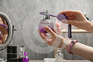 Woman holding luxurious perfume in crystal vintage bottle over dressing table,