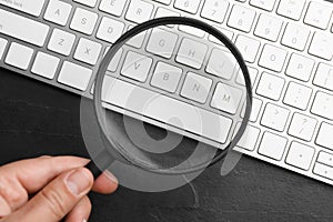 Woman holding magnifier glass over keyboard on black slate table. Find keywords concept