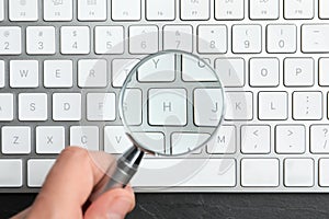 Woman holding magnifier glass over keyboard on slate table, top view. Find keywords concept