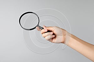 Woman holding magnifying glass on grey background  closeup. Find keywords concept
