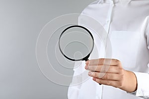 Woman holding magnifying glass on grey background  closeup. Find keywords concept