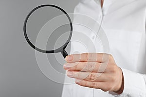 Woman holding magnifying glass on grey background  closeup. Find keywords concept