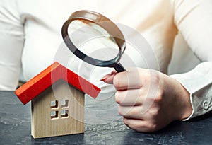 A woman is holding a magnifying glass over a wooden house. Real estate appraiser. Assessment of the condition of the house.