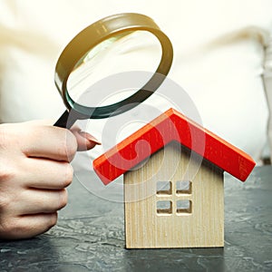 A woman is holding a magnifying glass over a wooden house. Real estate appraiser. Assessment of the condition of the house. photo