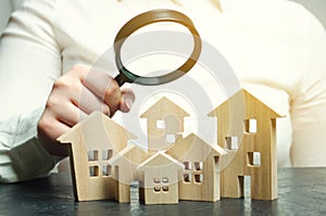A woman is holding a magnifying glass over a wooden houses. Real estate appraiser. Property valuation / appraisal. Find a house. photo