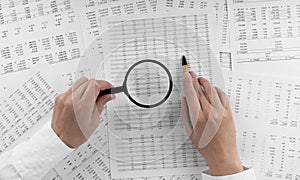 Woman holding a magnifying glass pointing at numbers on financial documents. ?oncept of finance, search and accounting.