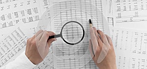 Woman holding a magnifying glass pointing at numbers on financial documents. ?oncept of finance, search and accounting