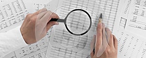 Woman holding a magnifying glass pointing at numbers on financial documents. ?oncept of finance, search and accounting