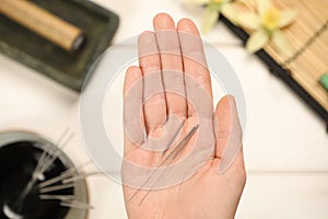 Woman holding many acupuncture needles over white wooden table, closeup