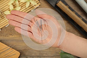 Woman holding many acupuncture needles over wooden table, closeup