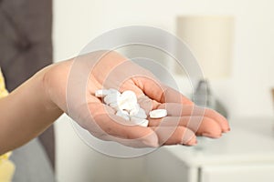 Woman holding many pills in hand indoors