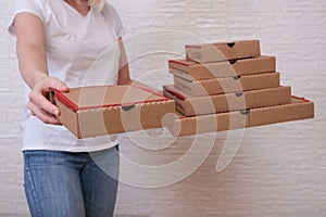 Woman holding many stacked carton pizza boxes of different sizes and offering, giving one to a customer, restaurant delivery