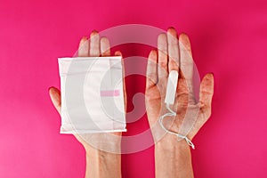 Woman holding menstrual tampon on a pink background. Menstruation time. Hygiene and protection