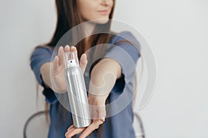 Woman holding metallic unbranded spray bottle with cosmetics in hands over gray background.