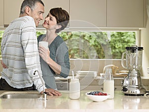 Woman Holding Milkshake While Looking At Husband In Kitchen