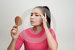 Woman holding a mirror, touch and worrying about her face