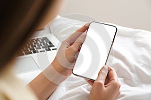 Woman holding mobile phone with empty screen in hands on bed at home, closeup