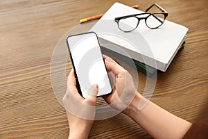 Woman holding mobile phone with empty screen at table, closeup