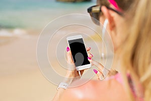 Woman holding mobile phone in hand and listening to music on earbuds