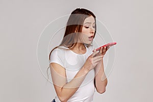 Woman holding mobile phone and talking into load speaker, making voice note, voice assistant.
